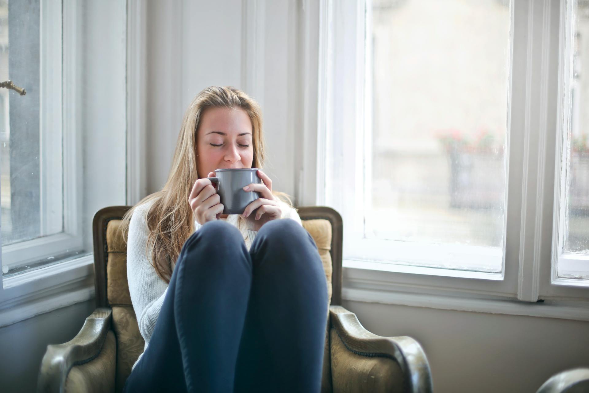 woman sits with her knees up enjoying a cup